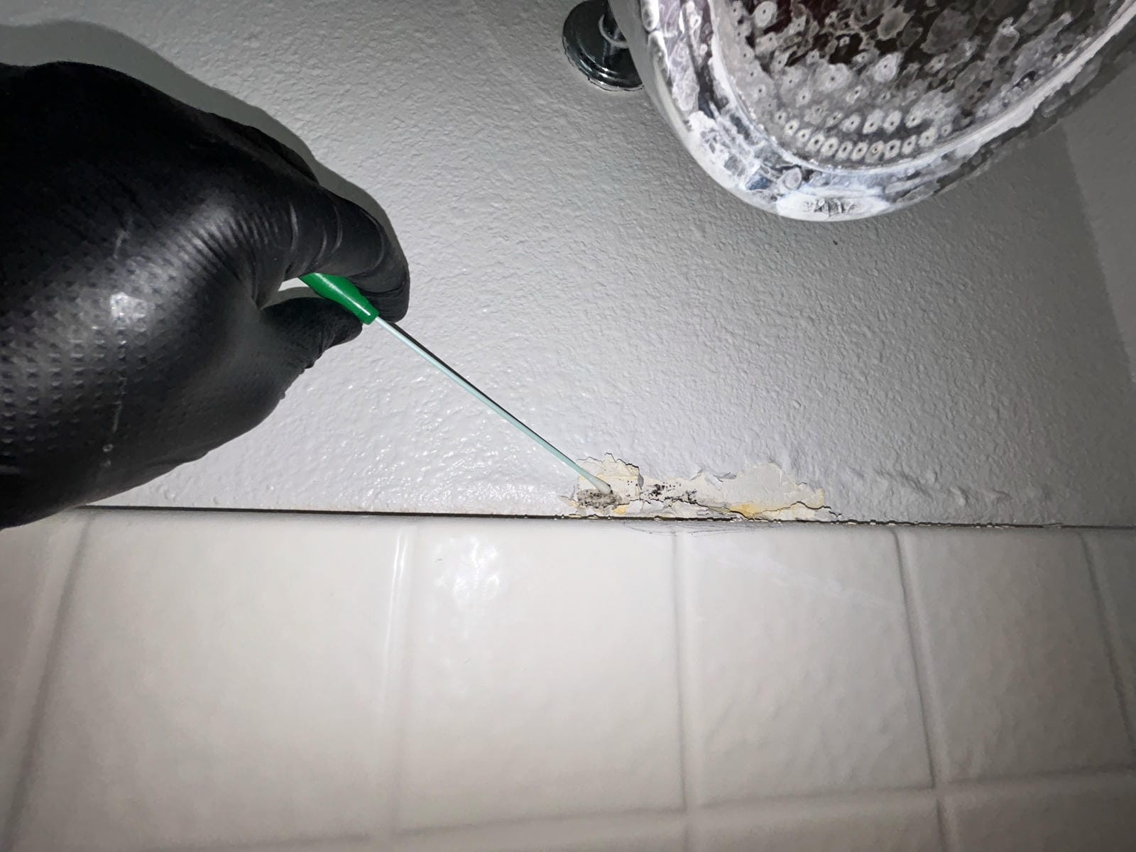 Inspector Examining Peeling Paint And Hidden Mold Above Shower Tiles In Newport Beach Bathroom.