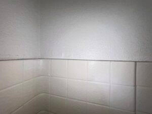 Close-up of bathroom wall corner in Orange County with early signs of mold and moisture damage above shower tiles.