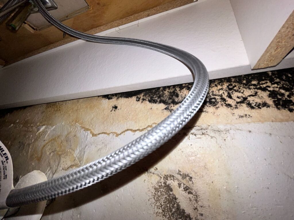 Wider Shot Of The Underside Of A Kitchen Sink Cabinet Revealing Significant Mold And Water Damage On The Back Wall.