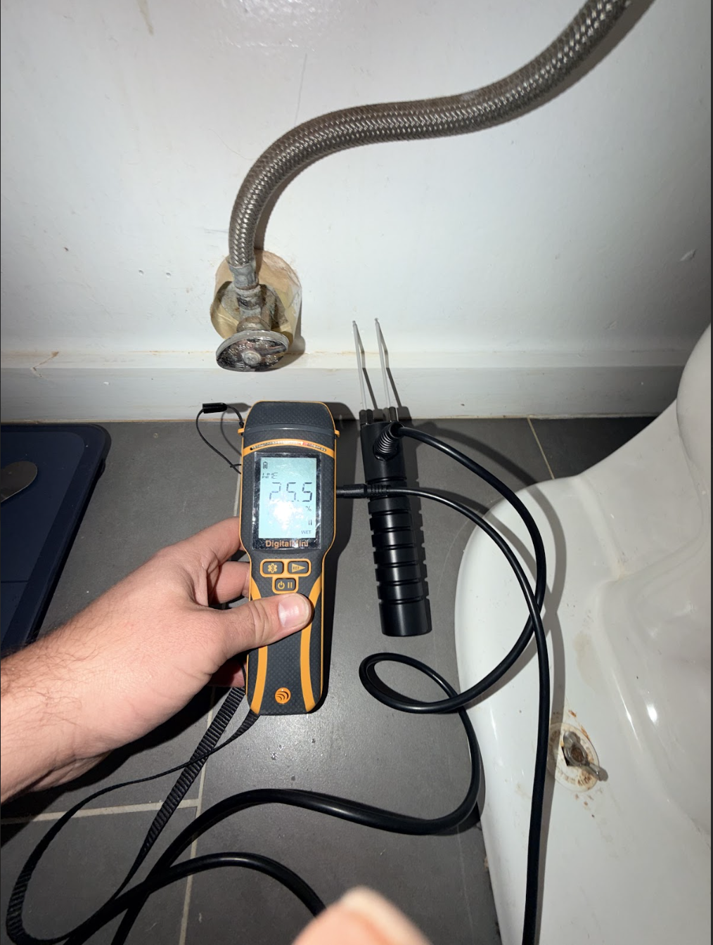 User-Inserted A Person Uses A Digital Meter Beside A Toilet, Likely Checking For Leaks Or Monitoring Water Efficiency.