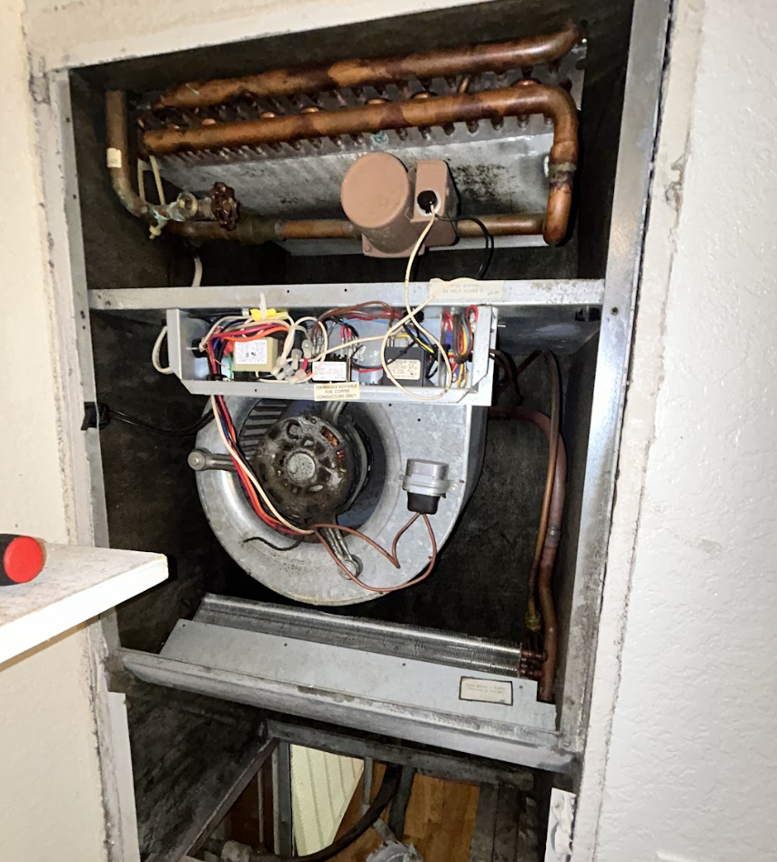 View Of An Exposed Hvac Unit In A Wall, Showing Copper Pipes, A Large Motor, And Colorful Wiring. The Scene Suggests Maintenance In Progress.
