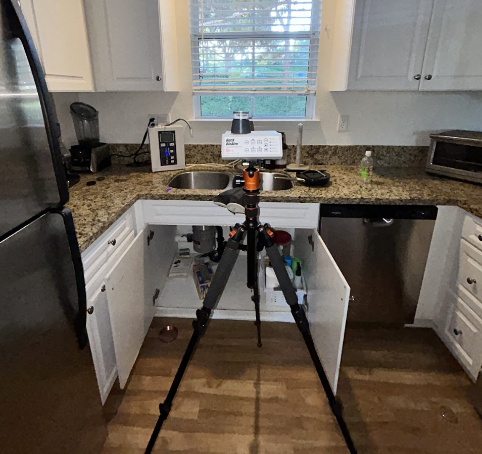 A Kitchen Scene With A Tripod In Front Of An Open Cabinet Under The Sink. Countertops Hold A Toaster And Blender, Conveying An Investigative Atmosphere.
