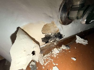 Wall corner with paint peeling away to expose a black mold patch and water-stained baseboard, found during a certified GPMI mold inspection in Orange County.